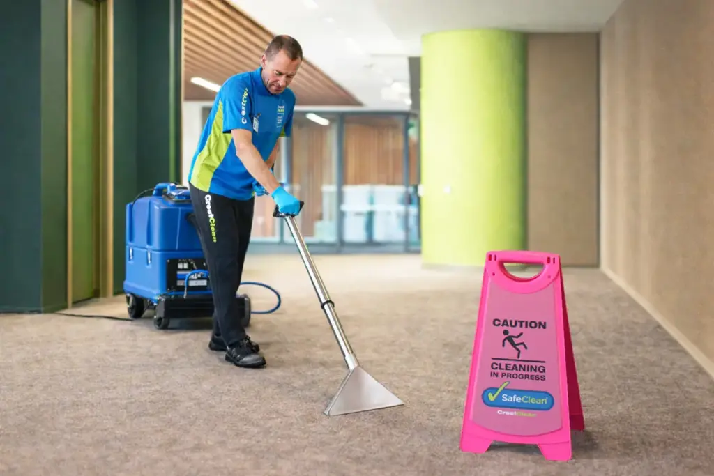 Commercial carpet cleaning in a modern hallway using professional extraction equipment with caution sign displayed.