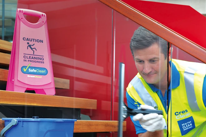 Window cleaner with cleaning in progress sign showing, and wearing safety vest