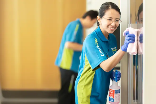 Cleaner wiping office kitchen refrigerator handle to sanitise